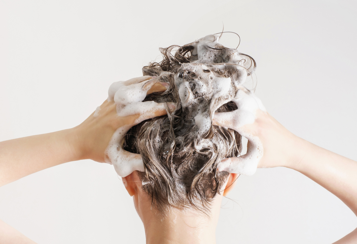 Woman lathering her hair in the shower with shampoo and using soft water vs. hard water.