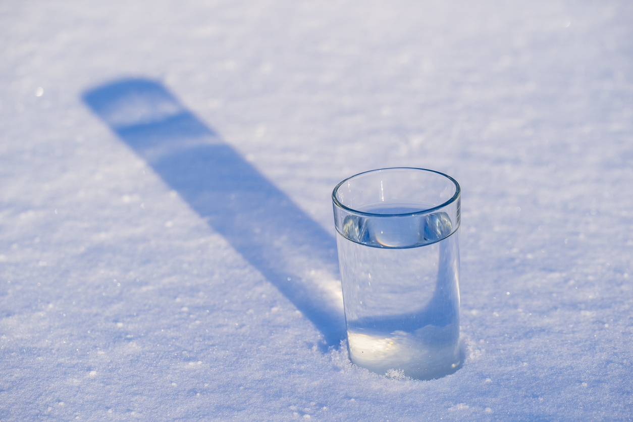 A glass of clear well water sitting in the snow.