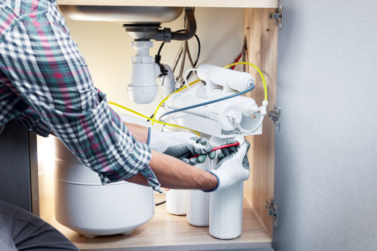 Plumber hand in gloves replace water filter cartridges at kitchen.